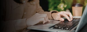 Hands typing on a laptop keyboard outdoors with a coffee cup nearby, representing planning and managing a network security strategy.