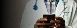 A healthcare professional wearing a lab coat and stethoscope uses a smartphone, representing digital communication, mobile technology, and modern workflows in healthcare services.