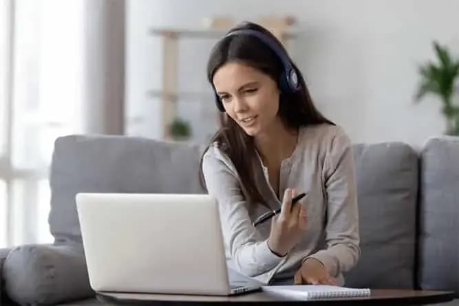 Woman wearing a headset using a laptop at home, participating in an online meeting or collaboration session using Microsoft Teams.