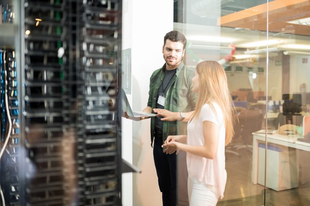 Two colleagues in front of a server rack, collaborating on an IT support ticketing system to enhance technical support processes.
